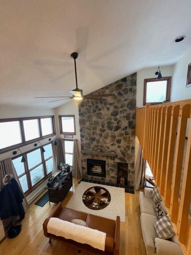 living room with vaulted ceiling, ceiling fan, light hardwood / wood-style floors, and a stone fireplace