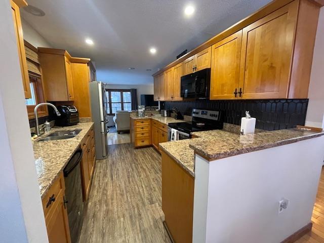 kitchen with black appliances, light hardwood / wood-style floors, kitchen peninsula, light stone counters, and sink