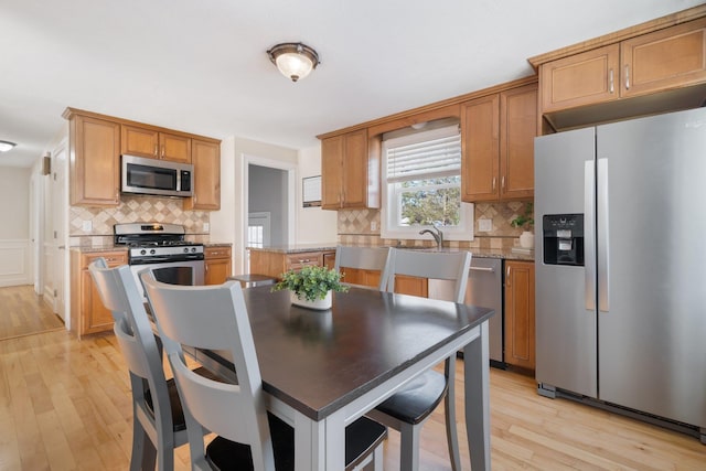 kitchen featuring appliances with stainless steel finishes, light hardwood / wood-style floors, light stone counters, and tasteful backsplash