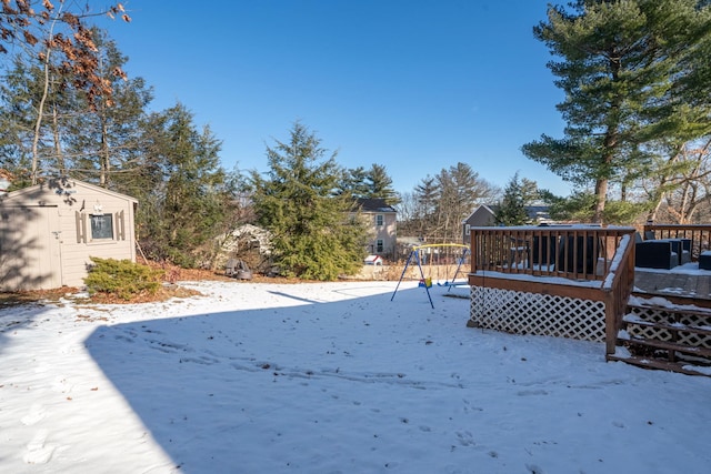 snowy yard featuring a playground, a storage shed, and a wooden deck