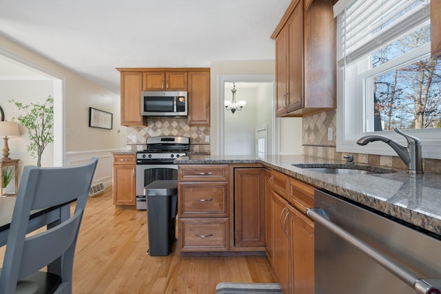 kitchen with stainless steel appliances, light wood-type flooring, stone countertops, backsplash, and sink