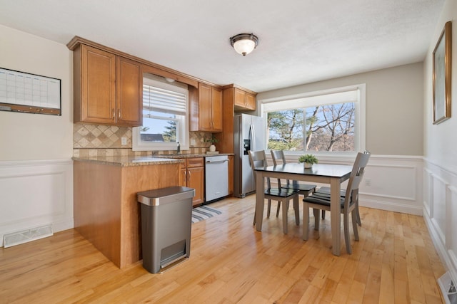 kitchen with appliances with stainless steel finishes, light hardwood / wood-style floors, light stone countertops, sink, and backsplash