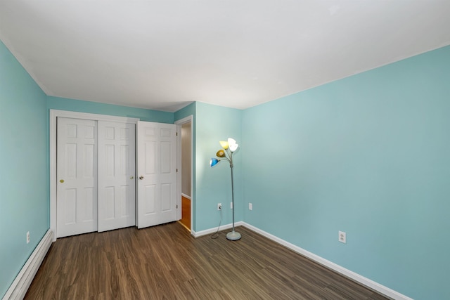 unfurnished bedroom featuring baseboard heating, dark hardwood / wood-style flooring, and a closet