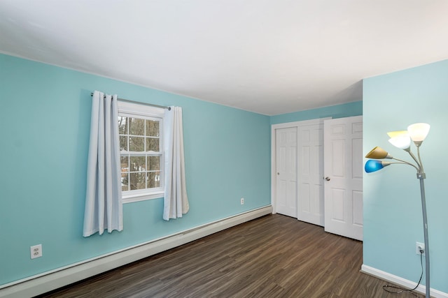 unfurnished bedroom featuring baseboard heating, a closet, and dark wood-type flooring