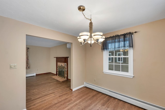 unfurnished dining area with a baseboard heating unit, a chandelier, hardwood / wood-style flooring, and a fireplace