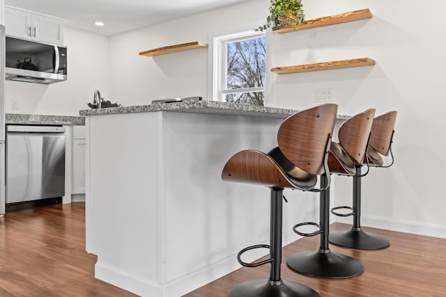 room details featuring stainless steel appliances, light stone countertops, dark hardwood / wood-style flooring, a kitchen bar, and white cabinets