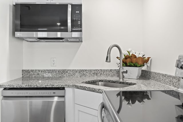 kitchen with stainless steel appliances, light stone countertops, white cabinets, and sink