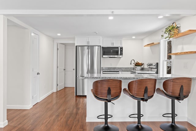 kitchen with stainless steel appliances, kitchen peninsula, light stone countertops, a breakfast bar, and white cabinets