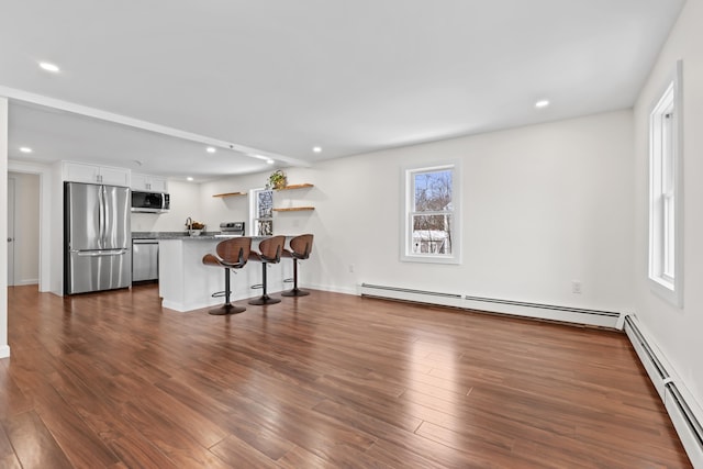 kitchen with white cabinets, stainless steel appliances, a baseboard radiator, and a kitchen breakfast bar