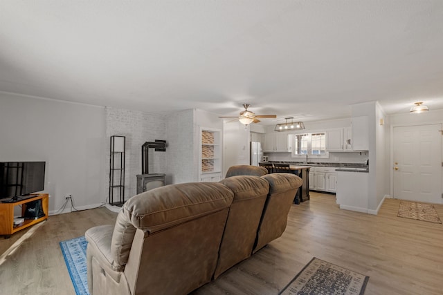 living room featuring light hardwood / wood-style floors, ceiling fan, sink, and a wood stove