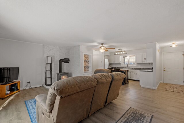 living room with sink, ceiling fan, light wood-type flooring, and a wood stove