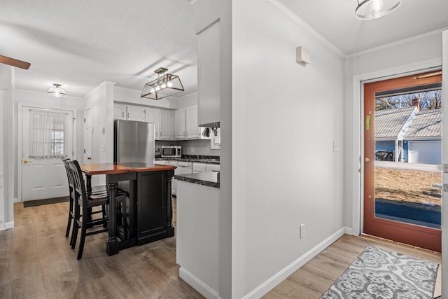 kitchen with white cabinetry, a breakfast bar area, appliances with stainless steel finishes, crown molding, and light hardwood / wood-style flooring