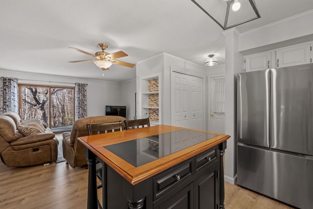 kitchen featuring stainless steel fridge, ceiling fan, white cabinetry, ornamental molding, and a kitchen breakfast bar