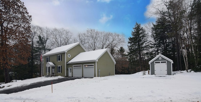 snow covered property with a storage unit and a garage