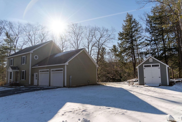 view of snowy exterior featuring a storage shed and a garage