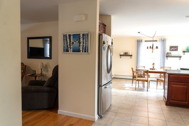 kitchen with a notable chandelier, stainless steel fridge, a baseboard heating unit, decorative light fixtures, and light tile patterned flooring