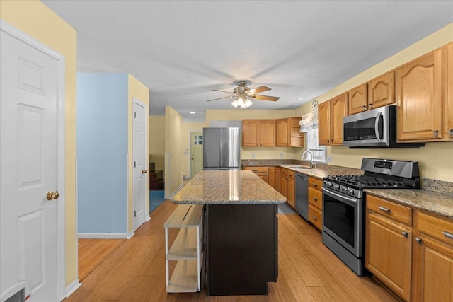 kitchen featuring sink, a center island, ceiling fan, light stone countertops, and appliances with stainless steel finishes