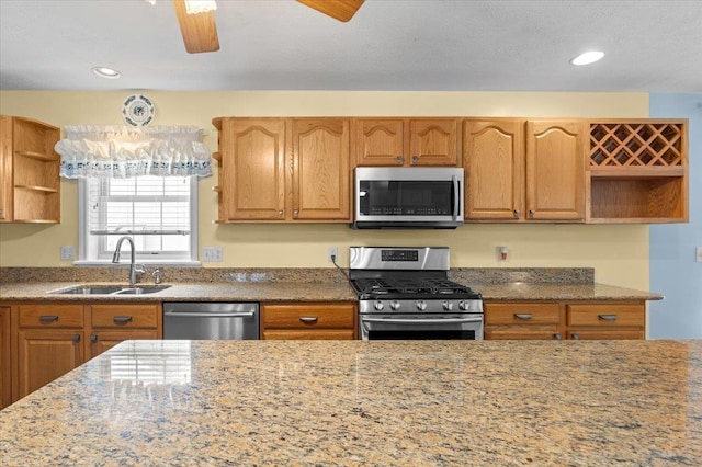 kitchen with stainless steel appliances, sink, ceiling fan, and light stone counters