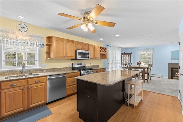 kitchen featuring appliances with stainless steel finishes, light hardwood / wood-style floors, a center island, a kitchen bar, and sink