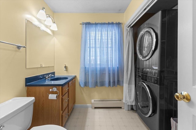 bathroom featuring toilet, a baseboard heating unit, stacked washer / dryer, and vanity