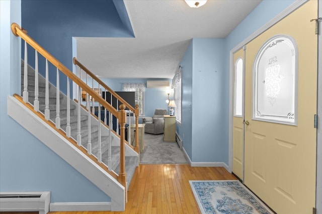 foyer entrance featuring wood-type flooring, a textured ceiling, baseboard heating, and a wall mounted AC