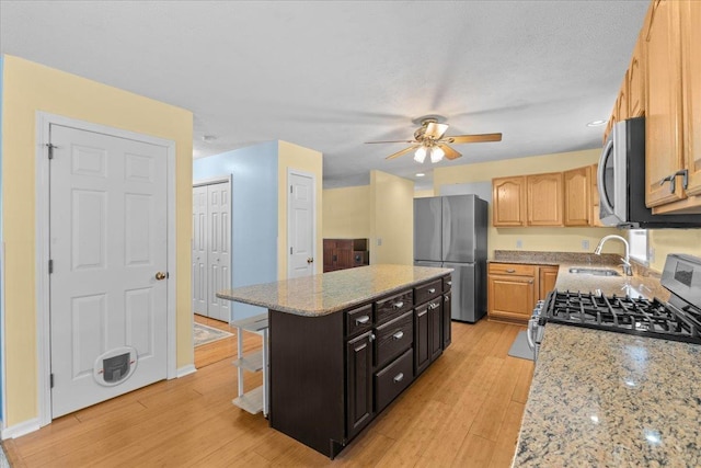 kitchen with light stone counters, a center island, appliances with stainless steel finishes, ceiling fan, and sink