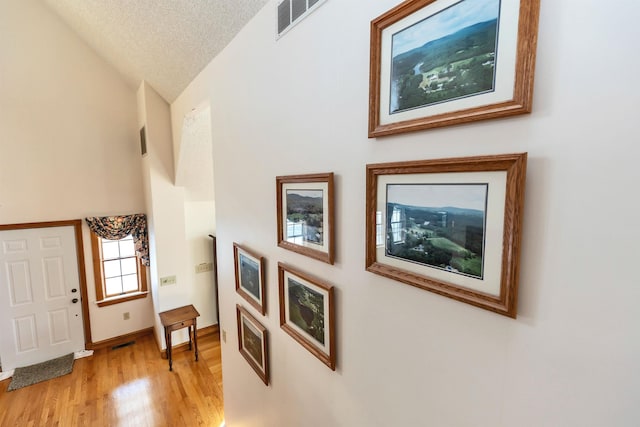 interior space with a textured ceiling, vaulted ceiling, and light wood-type flooring