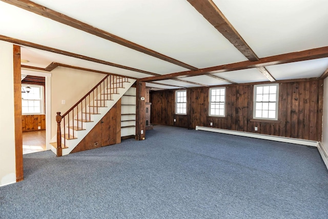 carpeted empty room with plenty of natural light, beamed ceiling, wooden walls, and a baseboard radiator