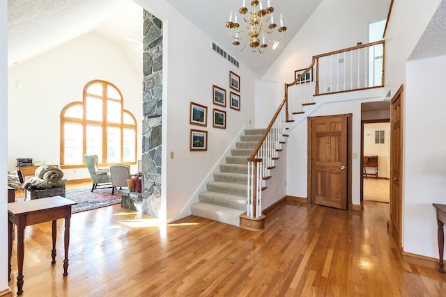 stairs featuring high vaulted ceiling, a textured ceiling, hardwood / wood-style flooring, and a chandelier