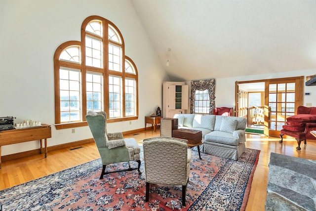 living room with high vaulted ceiling, a wealth of natural light, and light wood-type flooring