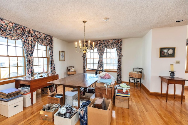 dining area with light hardwood / wood-style floors, a textured ceiling, and a notable chandelier