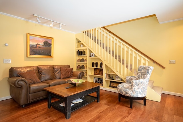 living room featuring built in shelves, rail lighting, ornamental molding, and hardwood / wood-style flooring