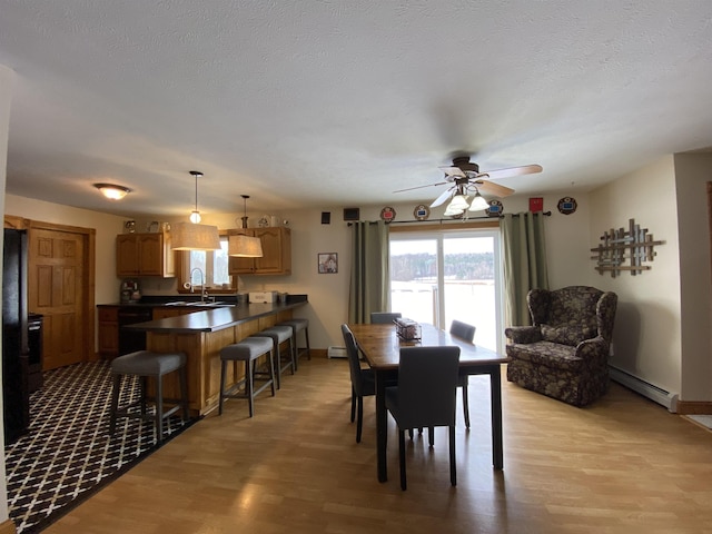 dining space featuring sink, baseboard heating, light wood-type flooring, and ceiling fan