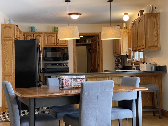 kitchen with kitchen peninsula, a breakfast bar area, black appliances, and hanging light fixtures