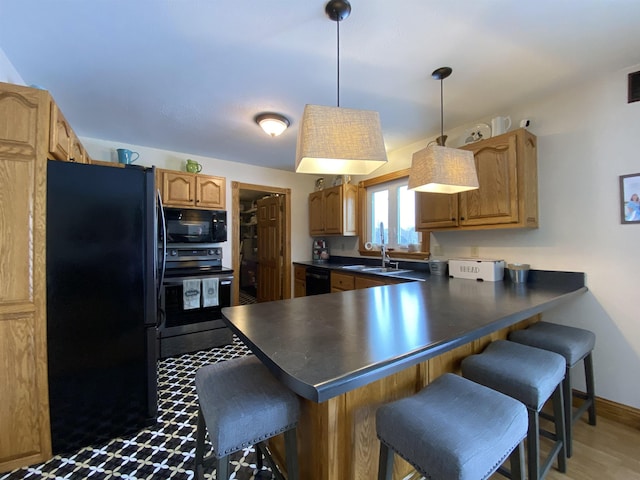 kitchen featuring black appliances, light hardwood / wood-style floors, kitchen peninsula, pendant lighting, and a breakfast bar