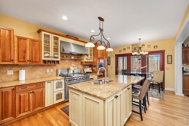 kitchen featuring double oven range, extractor fan, a center island with sink, hanging light fixtures, and sink