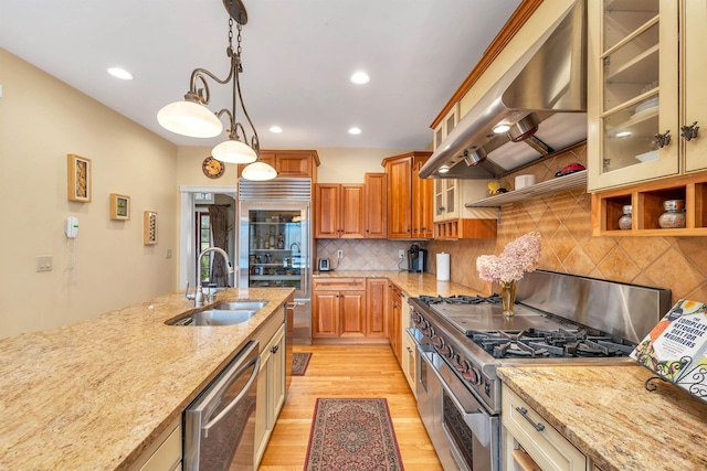 kitchen featuring high end appliances, ventilation hood, light stone countertops, and sink