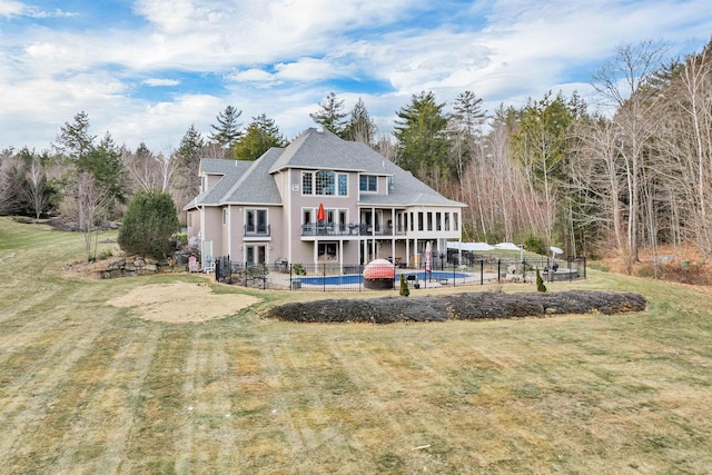 rear view of house with a balcony, a pool, and a lawn