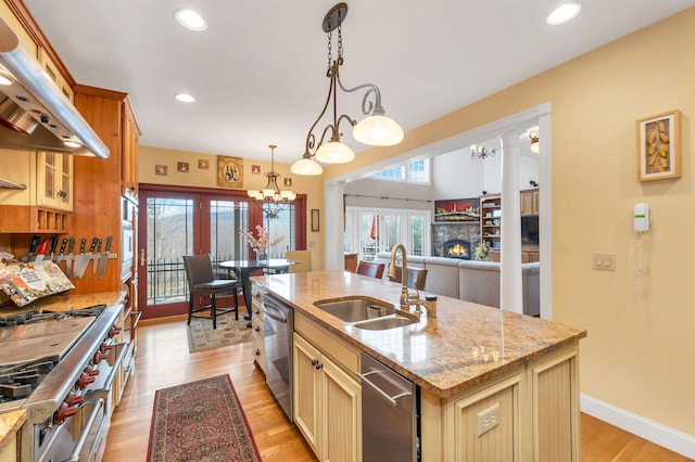 kitchen with exhaust hood, a fireplace, sink, hanging light fixtures, and a kitchen island with sink