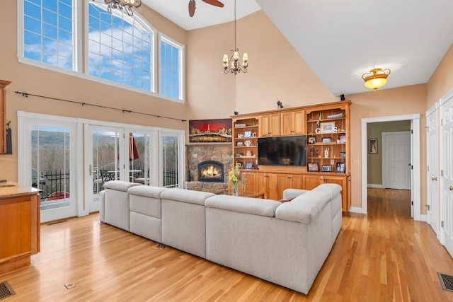 living room with ceiling fan with notable chandelier, light wood-type flooring, a towering ceiling, and a fireplace