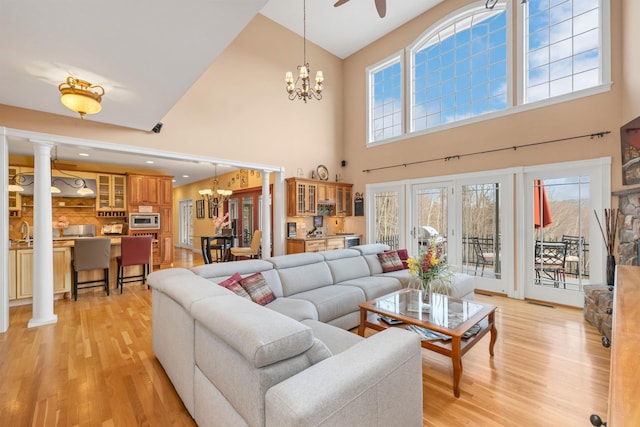 living room featuring ornate columns, a high ceiling, light wood-type flooring, ceiling fan with notable chandelier, and sink