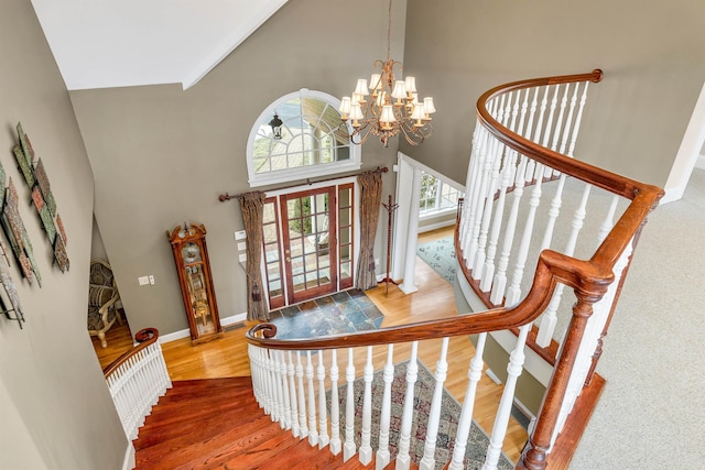 stairs featuring a chandelier, wood-type flooring, and high vaulted ceiling