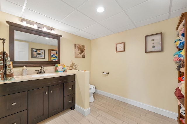 bathroom featuring toilet, vanity, a drop ceiling, and hardwood / wood-style flooring