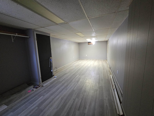 basement featuring hardwood / wood-style flooring, a baseboard heating unit, a paneled ceiling, and wooden walls