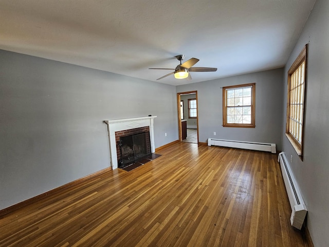 unfurnished living room featuring ceiling fan, a baseboard heating unit, a fireplace, and wood-type flooring