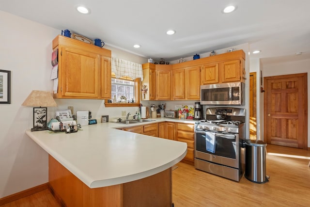 kitchen featuring light wood-style flooring, a peninsula, stainless steel appliances, light countertops, and a sink