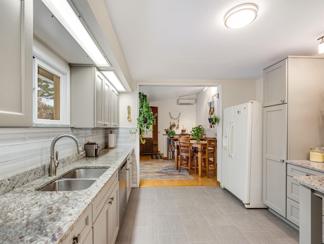 kitchen featuring a wall unit AC, decorative backsplash, light stone countertops, white refrigerator with ice dispenser, and sink