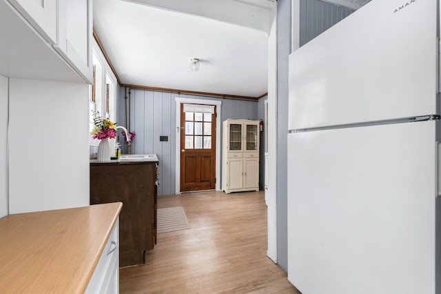 kitchen with white refrigerator, light hardwood / wood-style floors, sink, wood walls, and ornamental molding