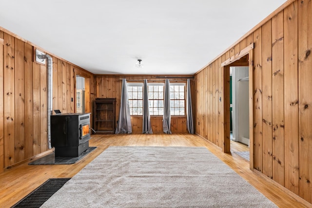 unfurnished living room featuring a wood stove, wood walls, and light wood-type flooring