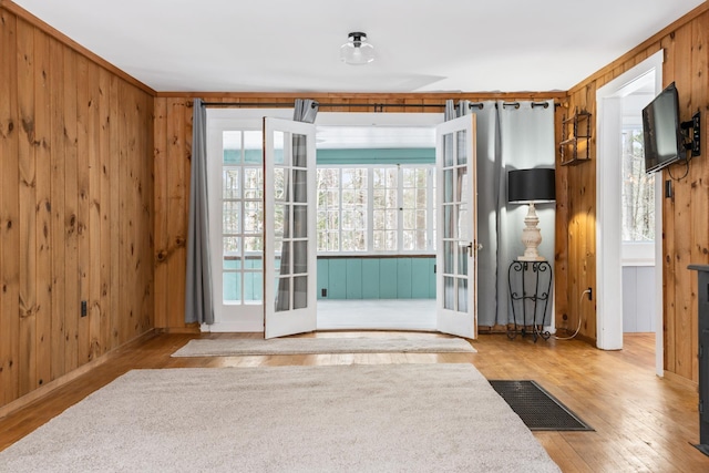 interior space with french doors, wooden walls, and light hardwood / wood-style floors